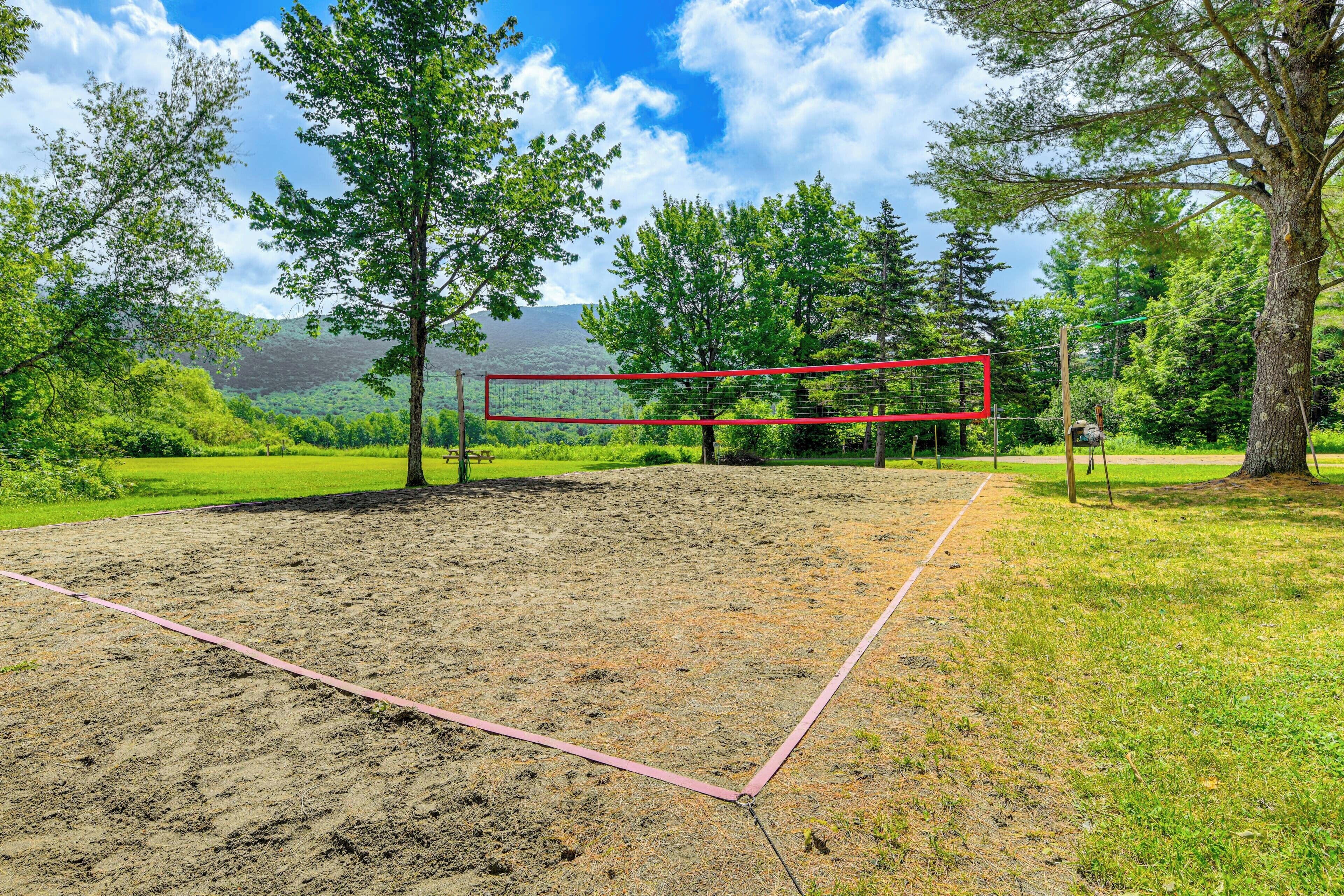 Un campo da pallavolo con rete rossa, circondato da alberi e da un prato.