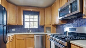 A kitchen with wooden cabinets, a stainless steel dishwasher, a gas stove, and a microwave. - Round Rock Home With Large Yard: 20 Mi to Austin! (Round Rock)
