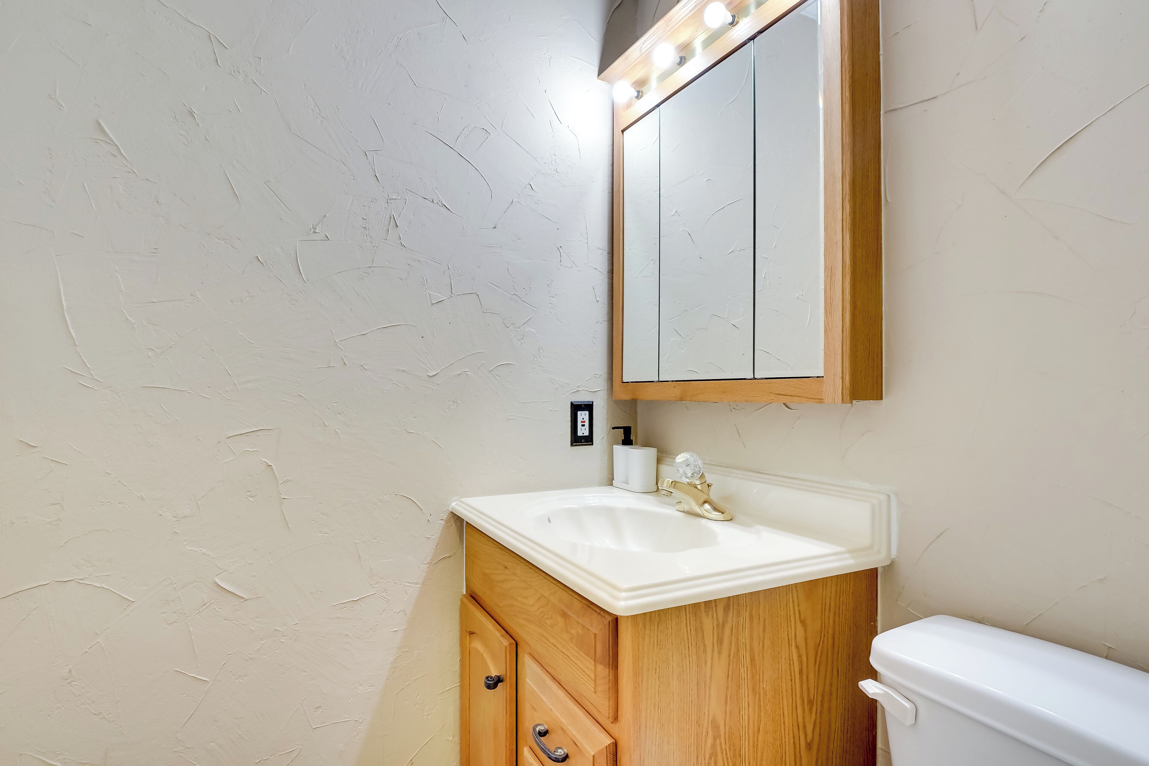 Une salle de bain avec un lavabo blanc, un meuble-lavabo en bois et un miroir avec éclairage intégré.