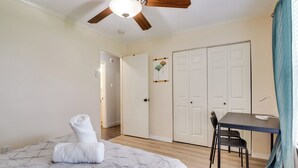 A bedroom with a bed, a ceiling fan, a desk with a chair, and a door. - Round Rock Home With Large Yard: 20 Mi to Austin! (Round Rock)
