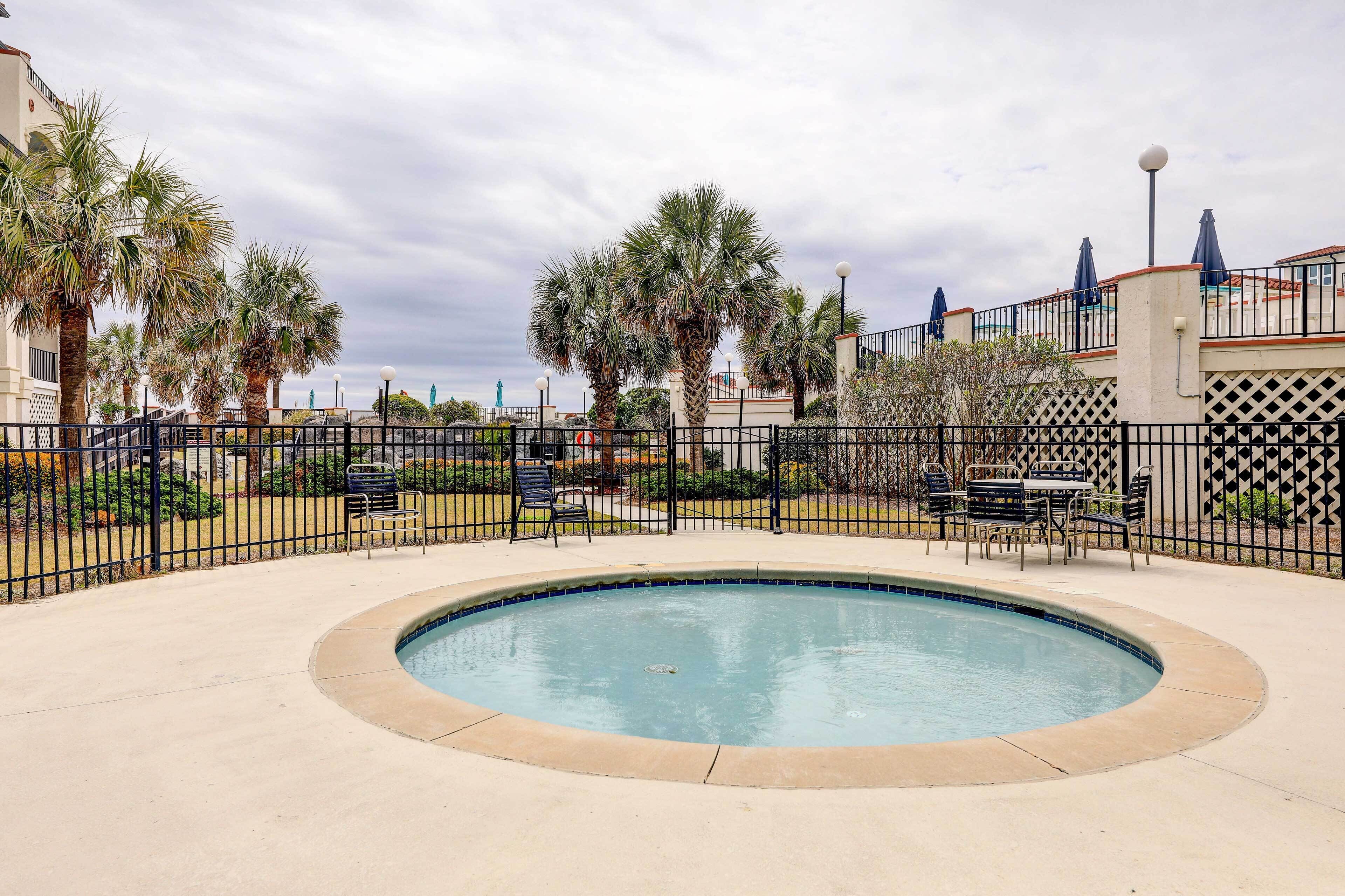 A swimming pool with a surrounding fence, palm trees, and outdoor seating.