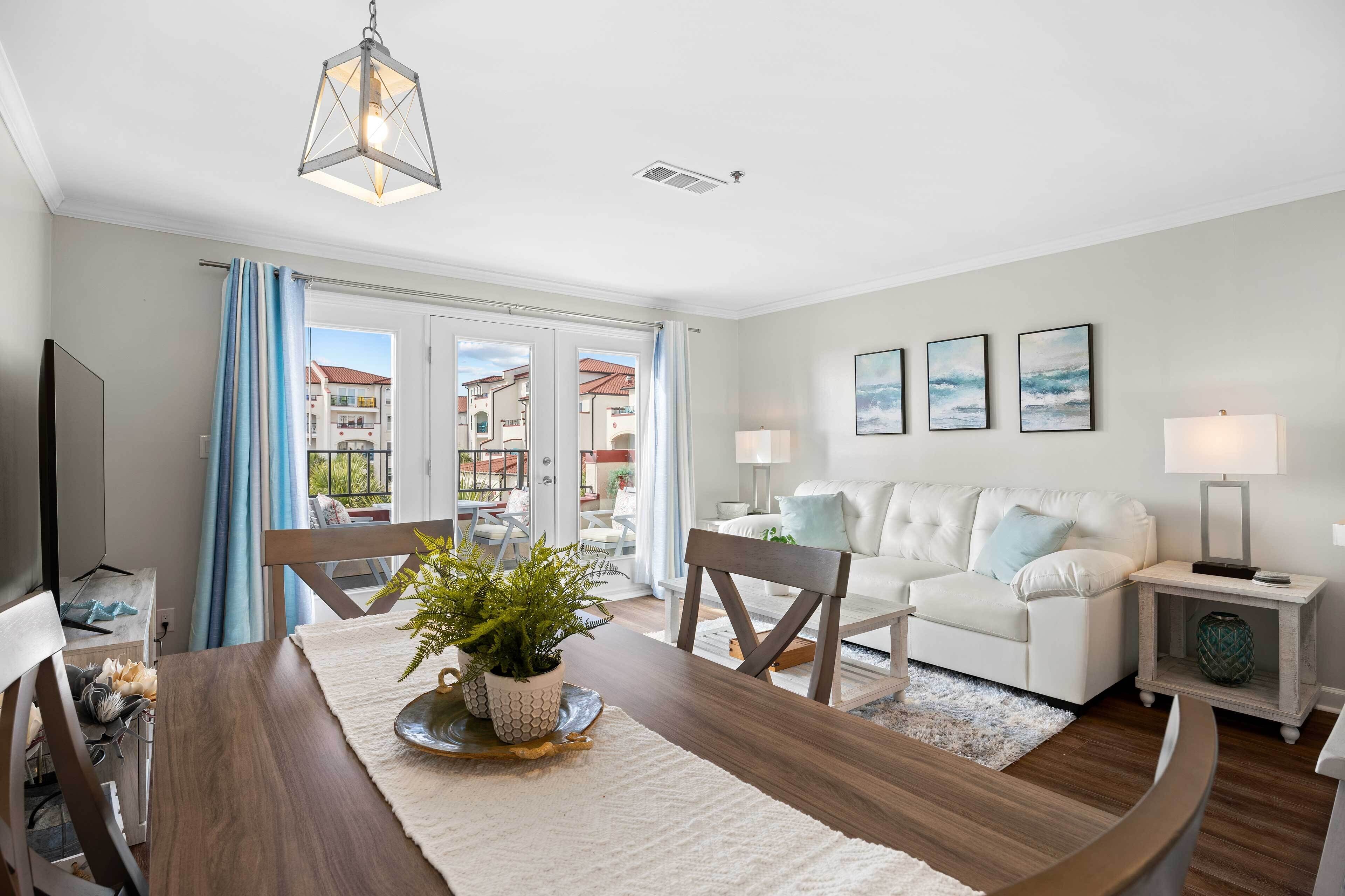 A modern living room with a wooden dining table, white sofa, and a TV.