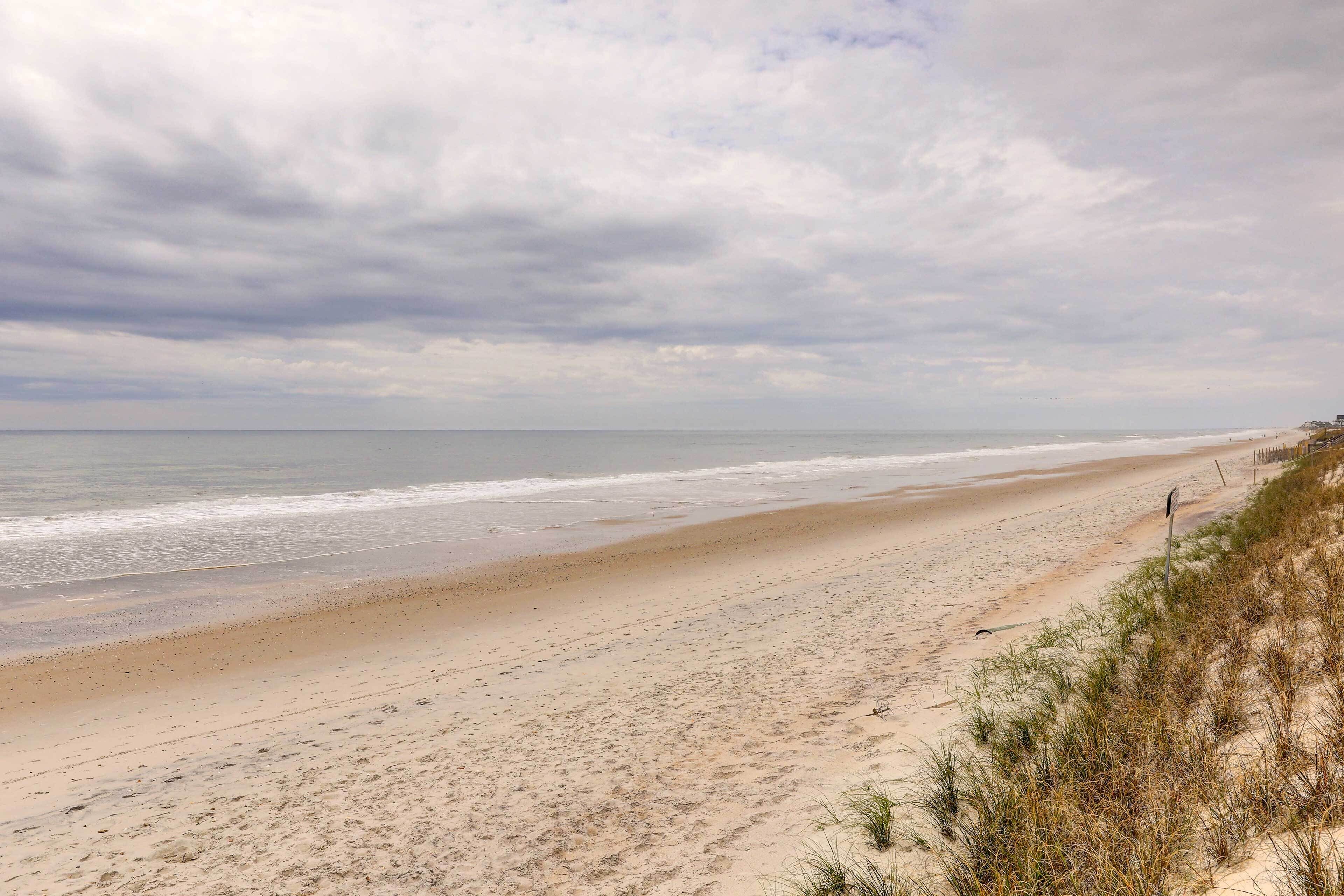 A wide sandy beach with gentle waves and a cloudy sky.