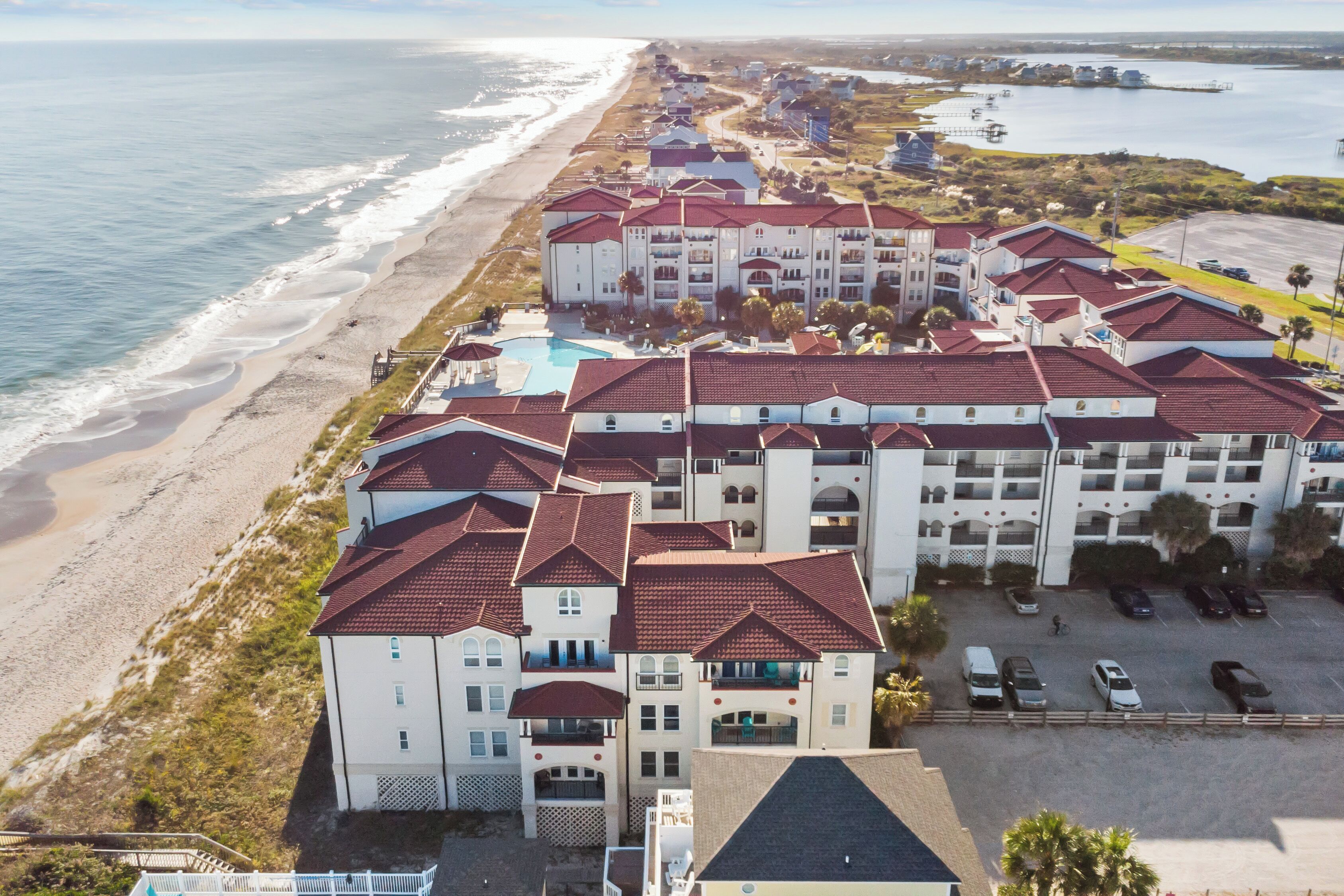 A beachfront hotel with multiple buildings, a parking lot, and a view of the ocean.