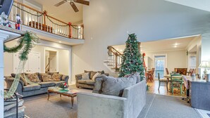 A spacious living room with a large gray sofa, a coffee table, and a Christmas tree. A staircase with a railing and a door is visible in the background. - 6 Mi to Bourbon Trail: Group Estate on 20 Acres (Shelbyville)