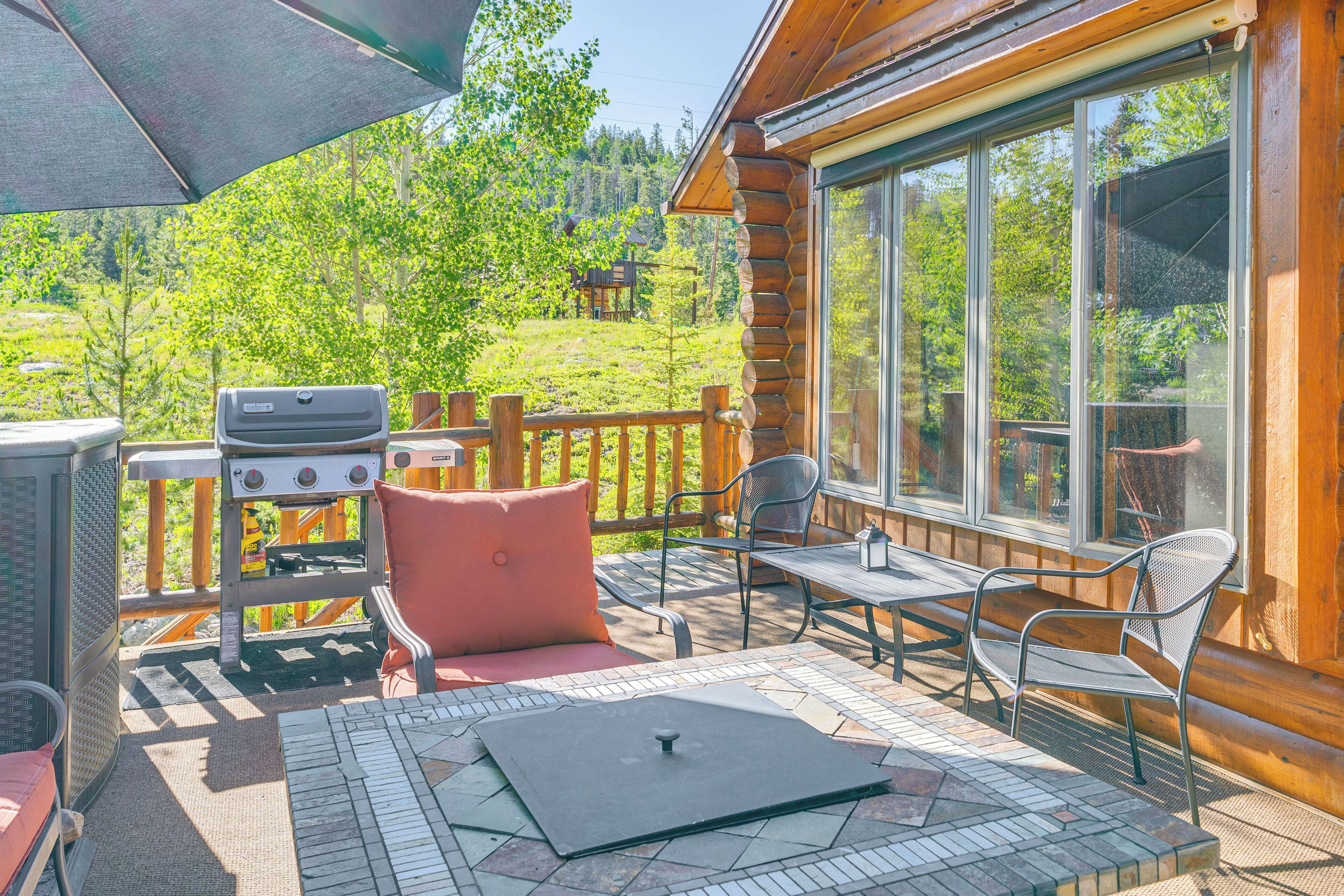Une terrasse en bois avec un barbecue, des sièges d’extérieur et une vue sur une zone boisée.
