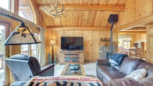 Ein gemütliches Blockhaus-Interieur mit Holzbalkendecke, einem großen Flachbildfernseher, Ledersofas und einem Kamin.