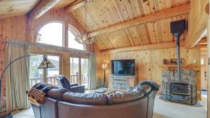 Ein gemütliches Blockhaus-Interieur mit Ledersofa, Fernseher, Kamin und großen Fenstern.