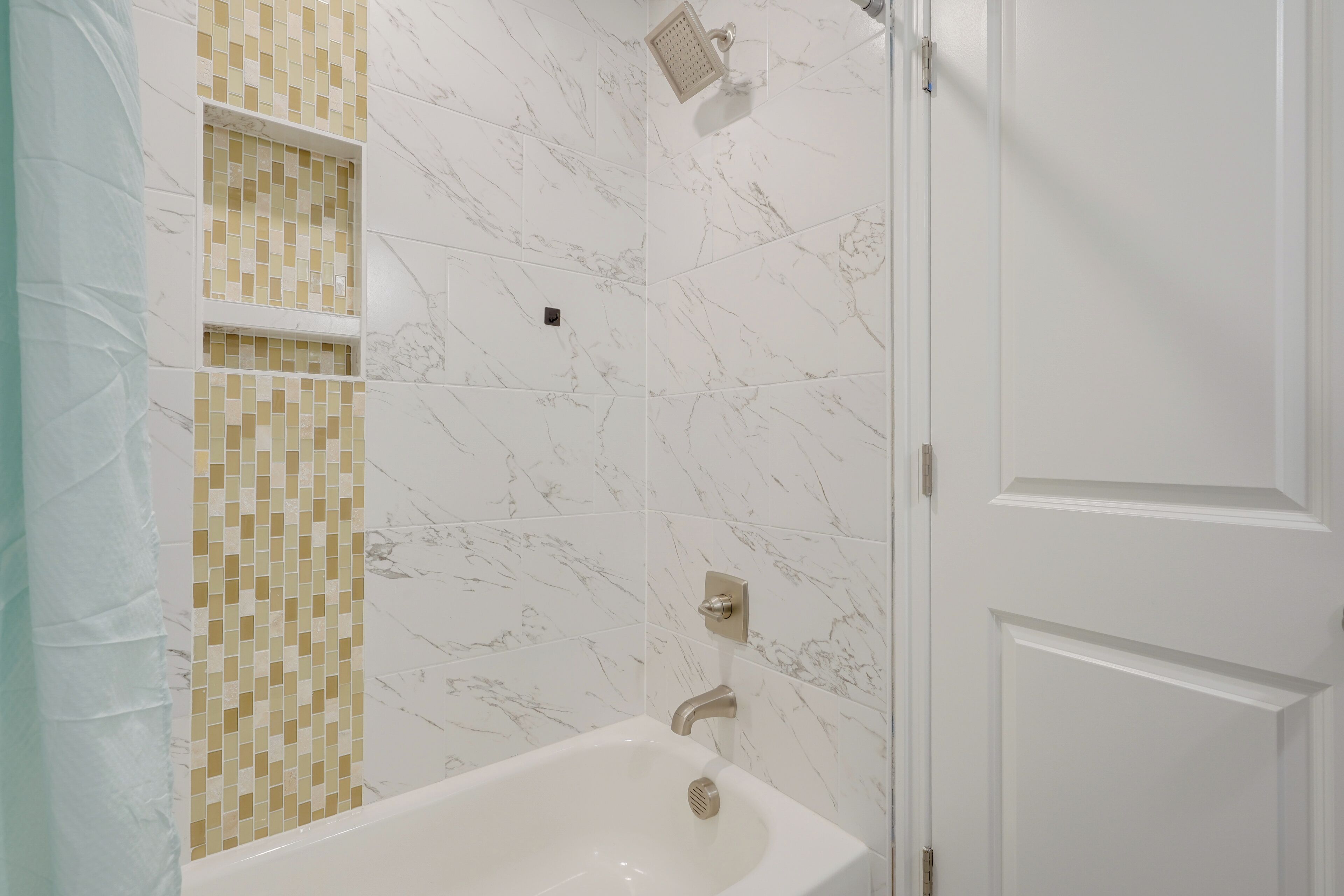 Un bagno con una vasca da bagno bianca, un angolo doccia e un rivestimento piastrellato con motivo a mosaico.
