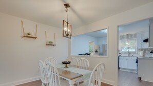 A dining area with a wooden table and white chairs, a hanging light fixture, and a view into the kitchen. - North Charleston Escape ~ 15 Mi to Dtwn Charleston (North Charleston)