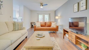 A living room with a beige sofa, a wooden coffee table, a leather couch, a TV on a wooden stand, and a ceiling fan. - North Charleston Escape ~ 15 Mi to Dtwn Charleston (North Charleston)