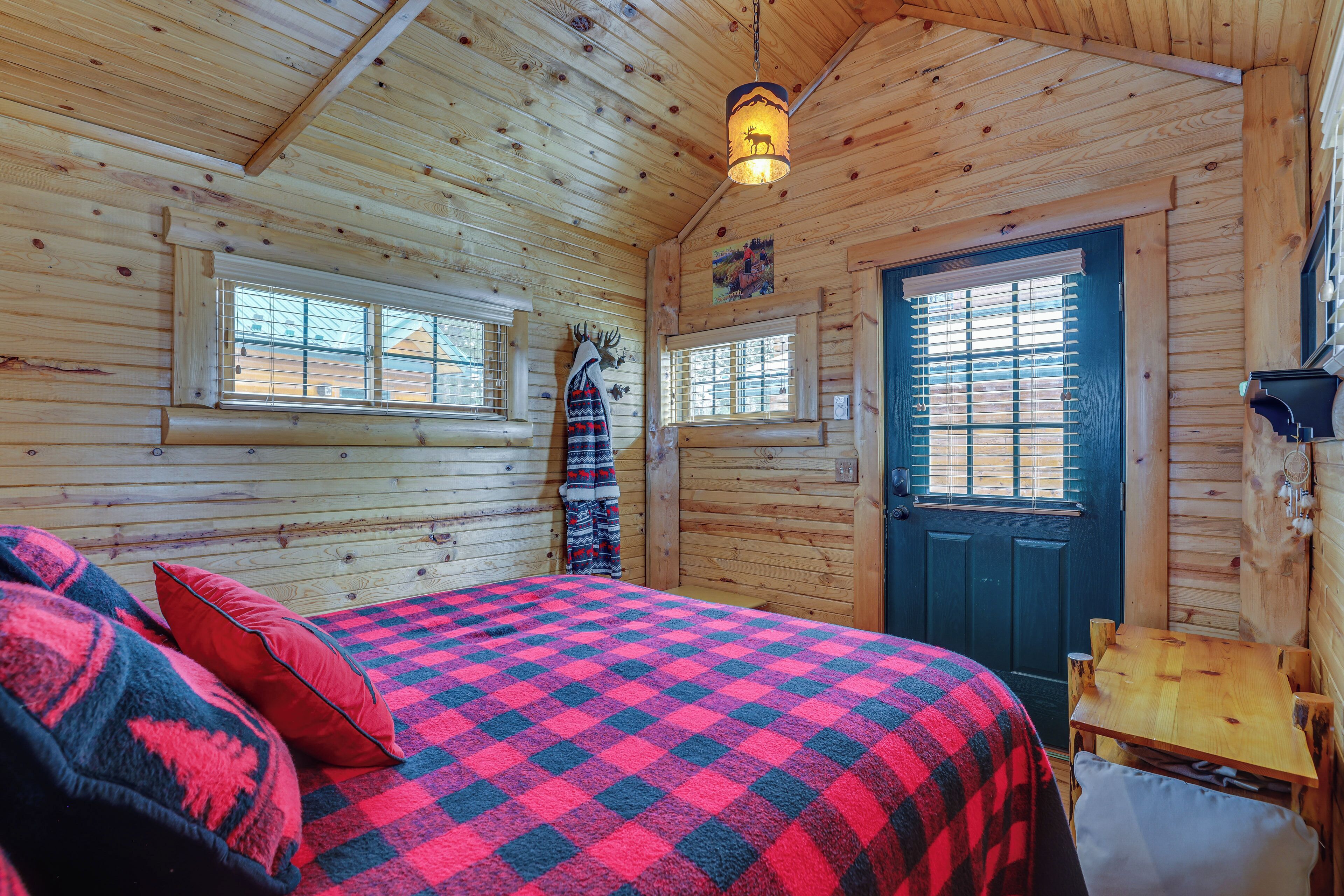 Une pièce chaleureuse dans un chalet en rondins, avec une couverture à carreaux sur le lit, une table en bois et une porte dotée d’une fenêtre.