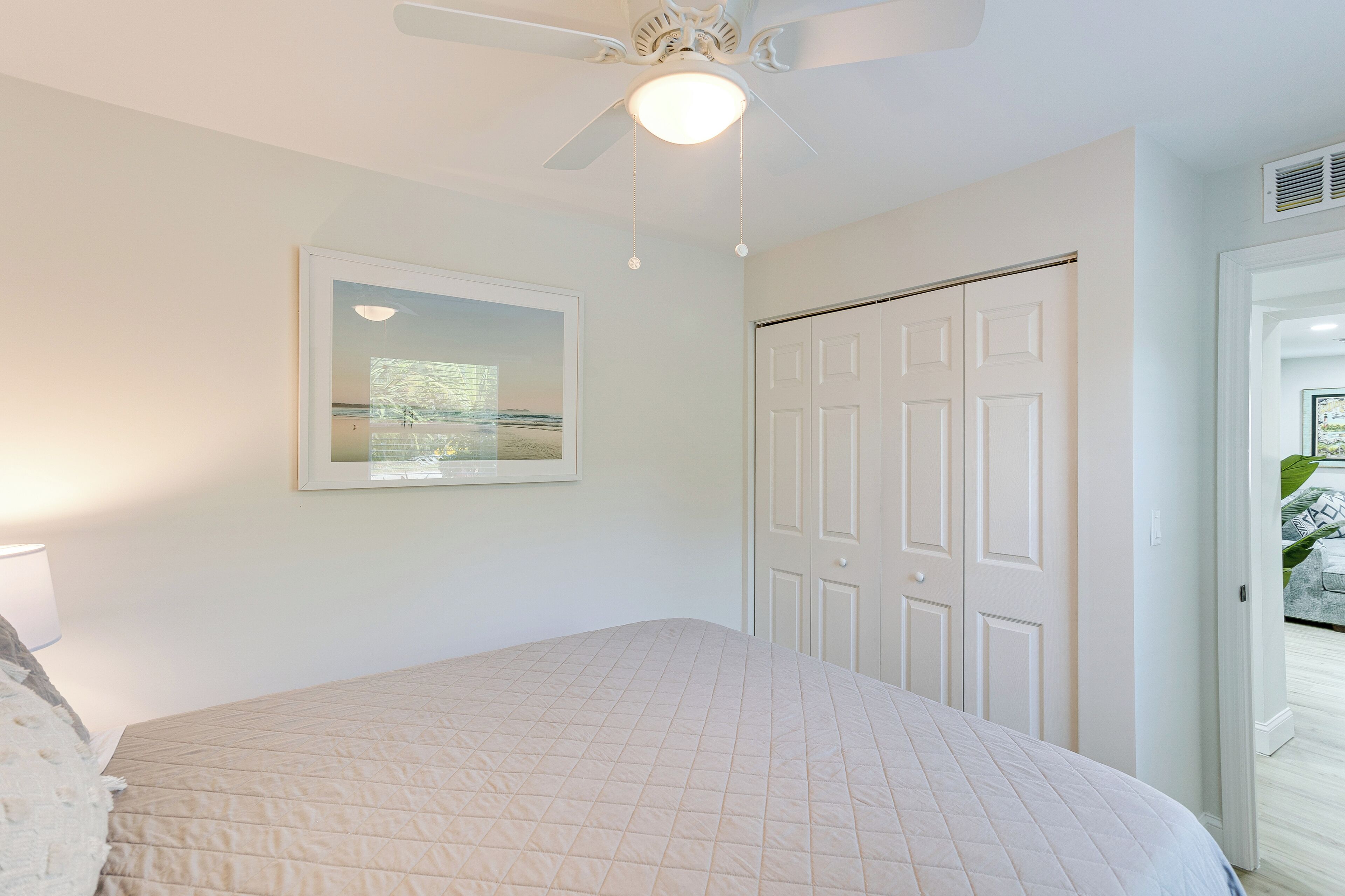 A bedroom with a bed, a ceiling fan, a door, and a framed picture on the wall.