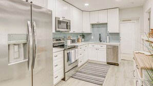 A modern kitchen with white cabinets, stainless steel appliances, a microwave, oven, and dishwasher. - Heated Pool + Backyard: North Palm Beach Retreat! (Juno Beach)