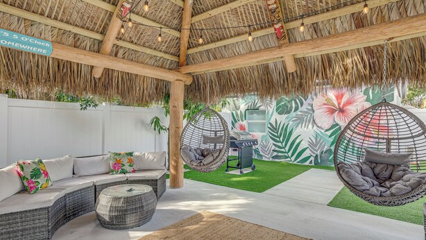 A covered outdoor seating area with a thatched roof, wicker furniture, and hanging chairs. - Heated Pool + Backyard: North Palm Beach Retreat! (Juno Beach)