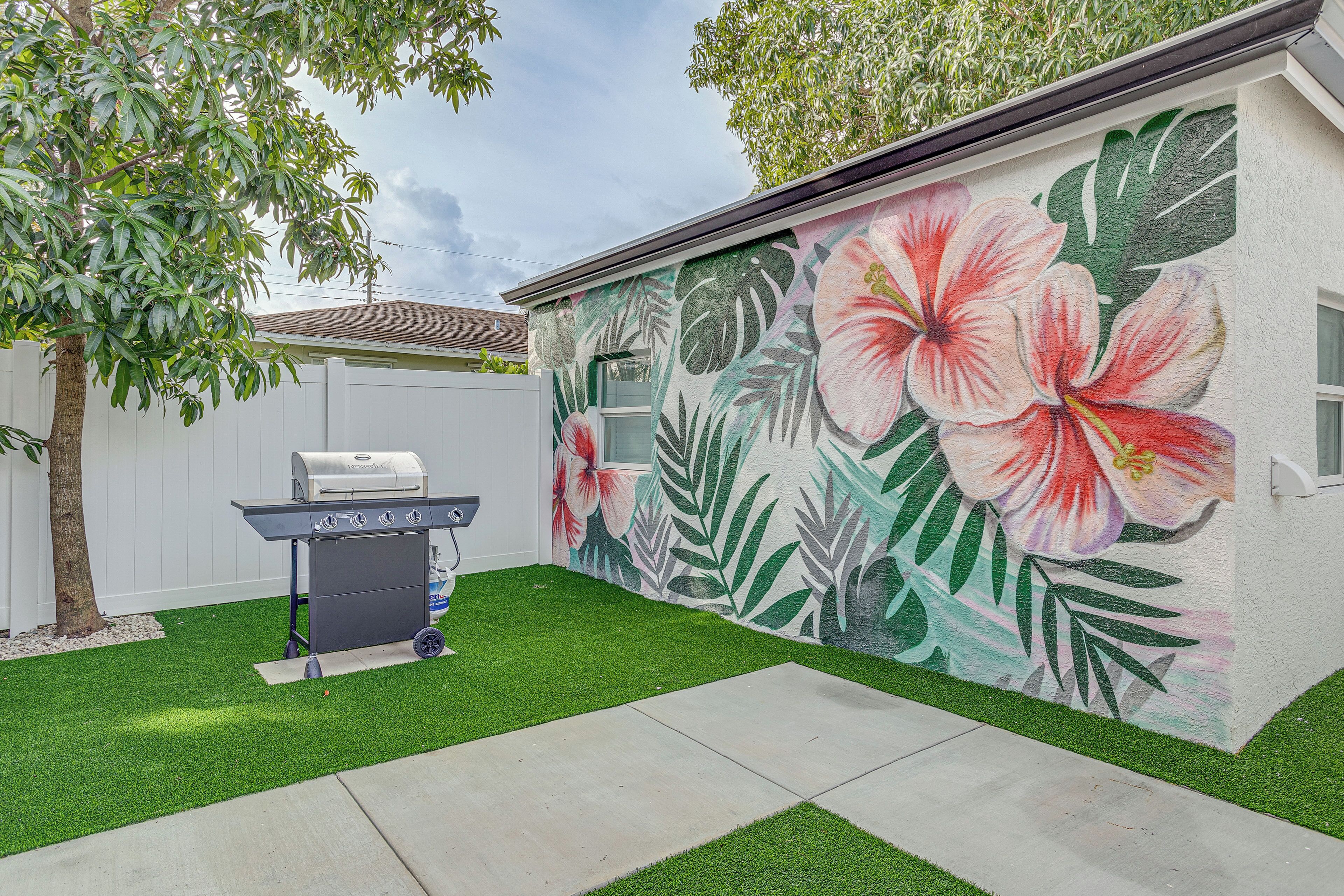 A backyard with artificial grass, a barbecue grill, and a wall mural of tropical flowers.