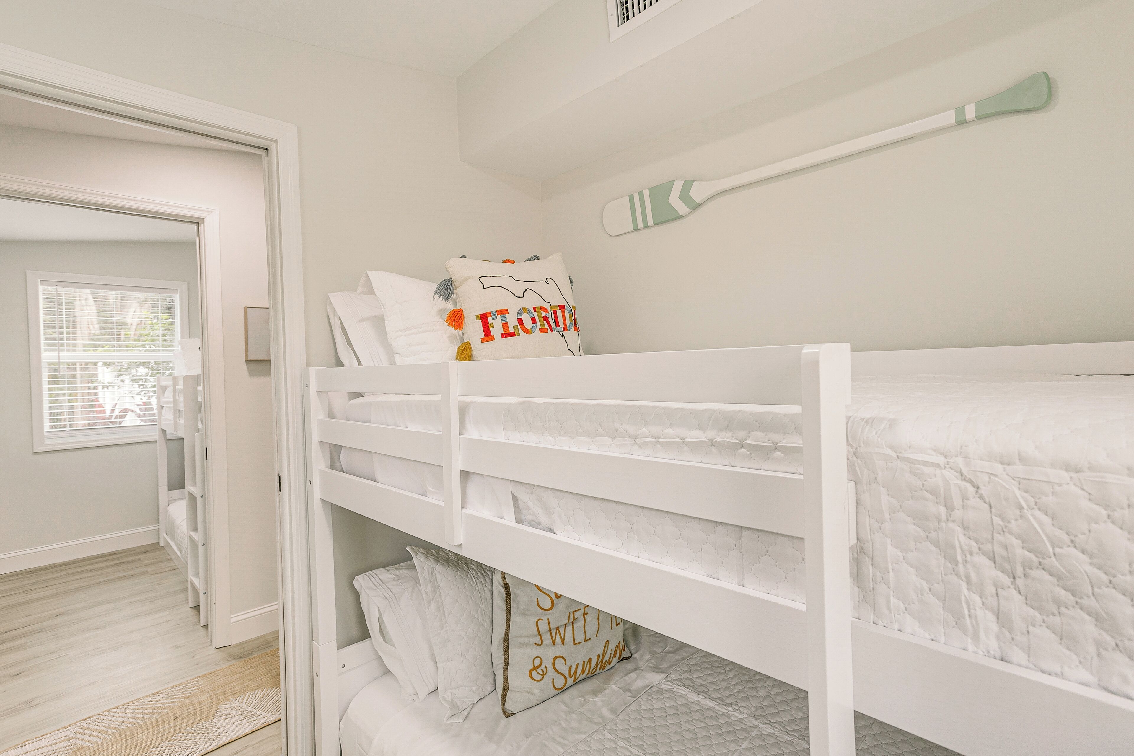 Habitación con literas, ropa de cama blanca y un cepillo de dientes colgado en la pared.