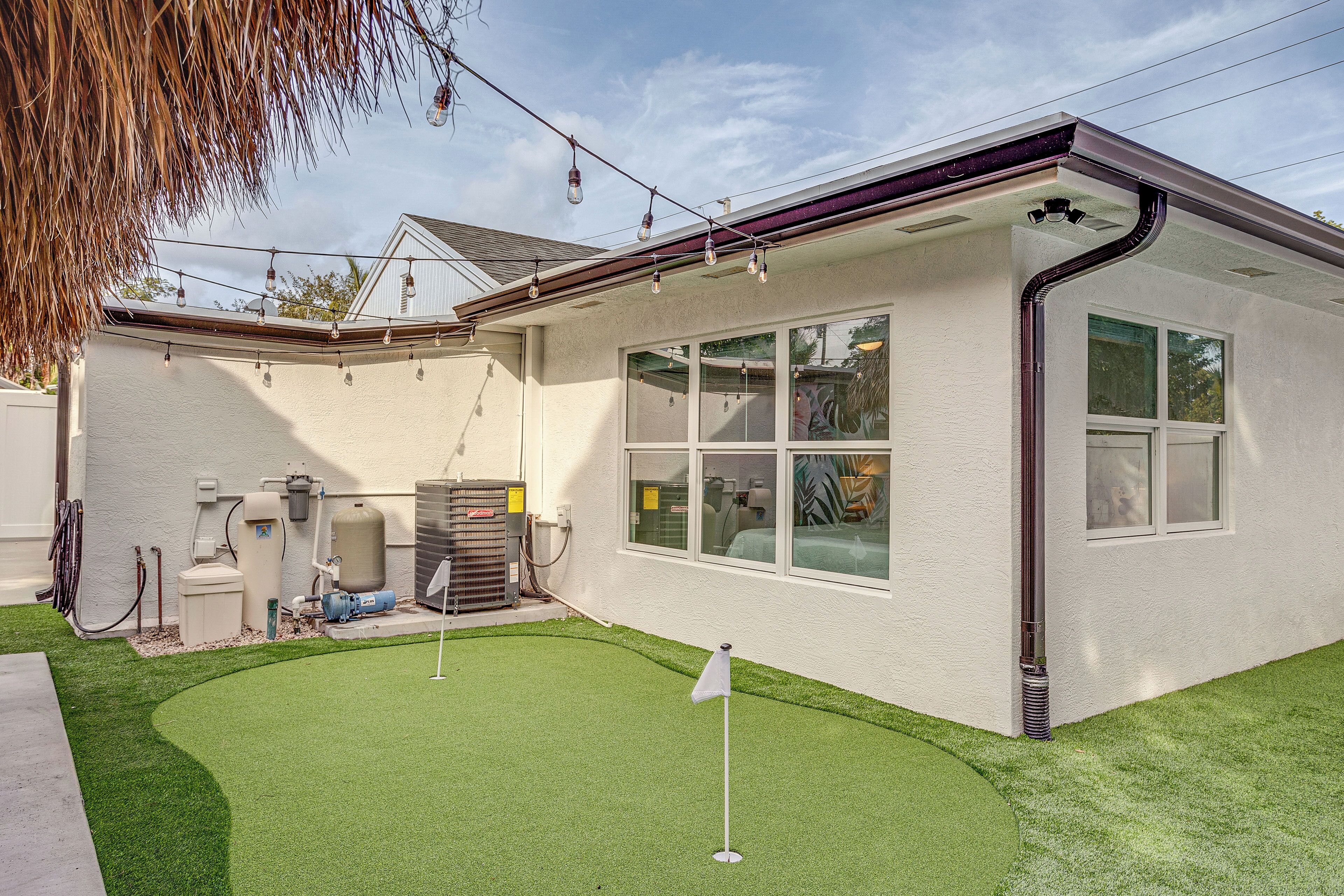 A house with a well-maintained lawn, a flagstick, and a water heater visible in the yard.