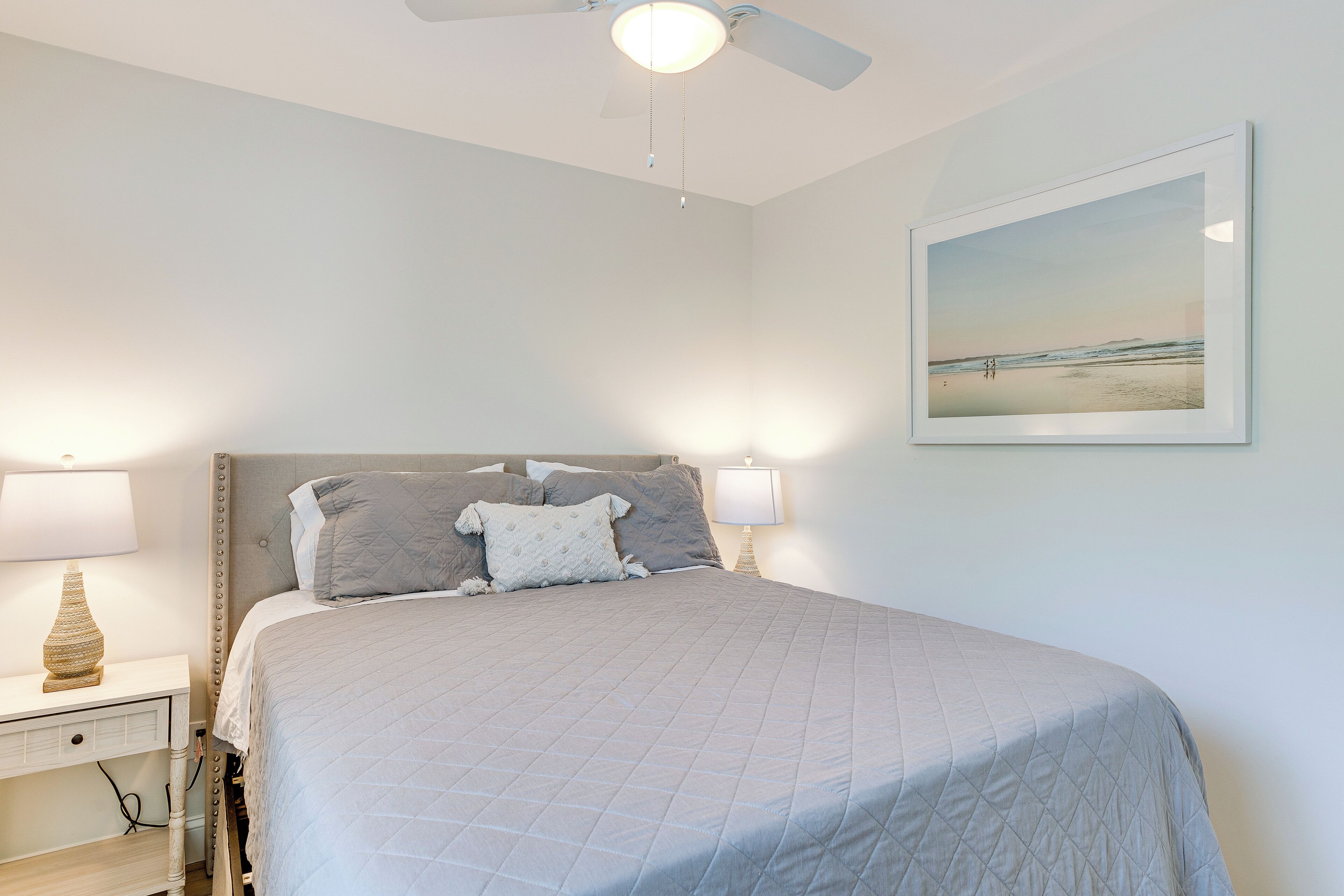 Une chambre à coucher avec un lit, des tables de chevet, un ventilateur de plafond et un tableau encadré au mur.