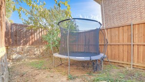Un giardino sul retro con un trampolino, una recinzione di legno e un muro in pietra.