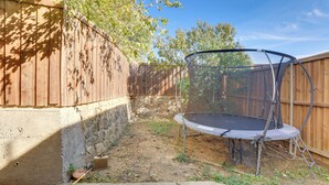 Un cortile con un trampolino, una recinzione in legno e un muro in pietra.