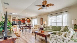 A spacious living room with a wooden coffee table, a green sofa, and a dining area with a wooden table and chairs. - Screened Lanai & Grill: Home in The Villages (Wildwood)