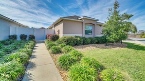 A modern two-story house with a covered driveway, well-maintained lawn, and various shrubs and plants. - Screened Lanai & Grill: Home in The Villages (Wildwood)