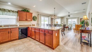 A spacious kitchen with wooden cabinets, a dishwasher, and a large island. There are multiple windows providing natural light and a ceiling fan for ventilation. - Screened Lanai & Grill: Home in The Villages (Wildwood)