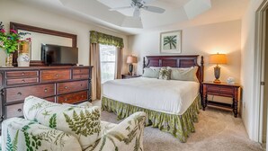 A bedroom with a bed, a dresser, a television, a ceiling fan, and a nightstand with a lamp. - Screened Lanai & Grill: Home in The Villages (Wildwood)