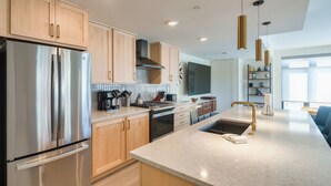 A modern kitchen with stainless steel appliances, wooden cabinets, and a large island with a sink and gold faucet. - Winter Park Condo w/ Hot Tub, Balcony & Shuttle! (Winter Park)