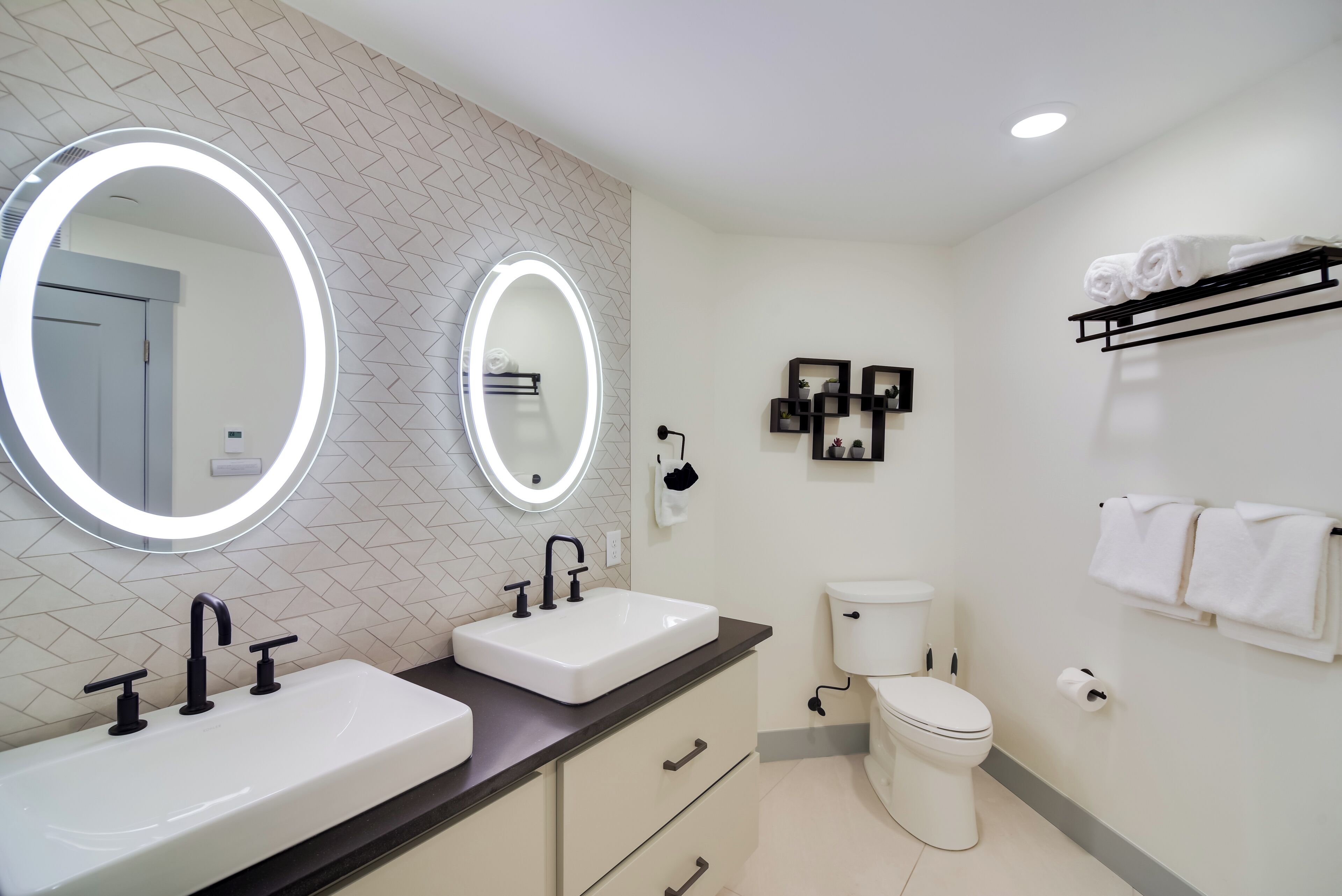 A modern bathroom with two sinks, a toilet, and a towel rack.