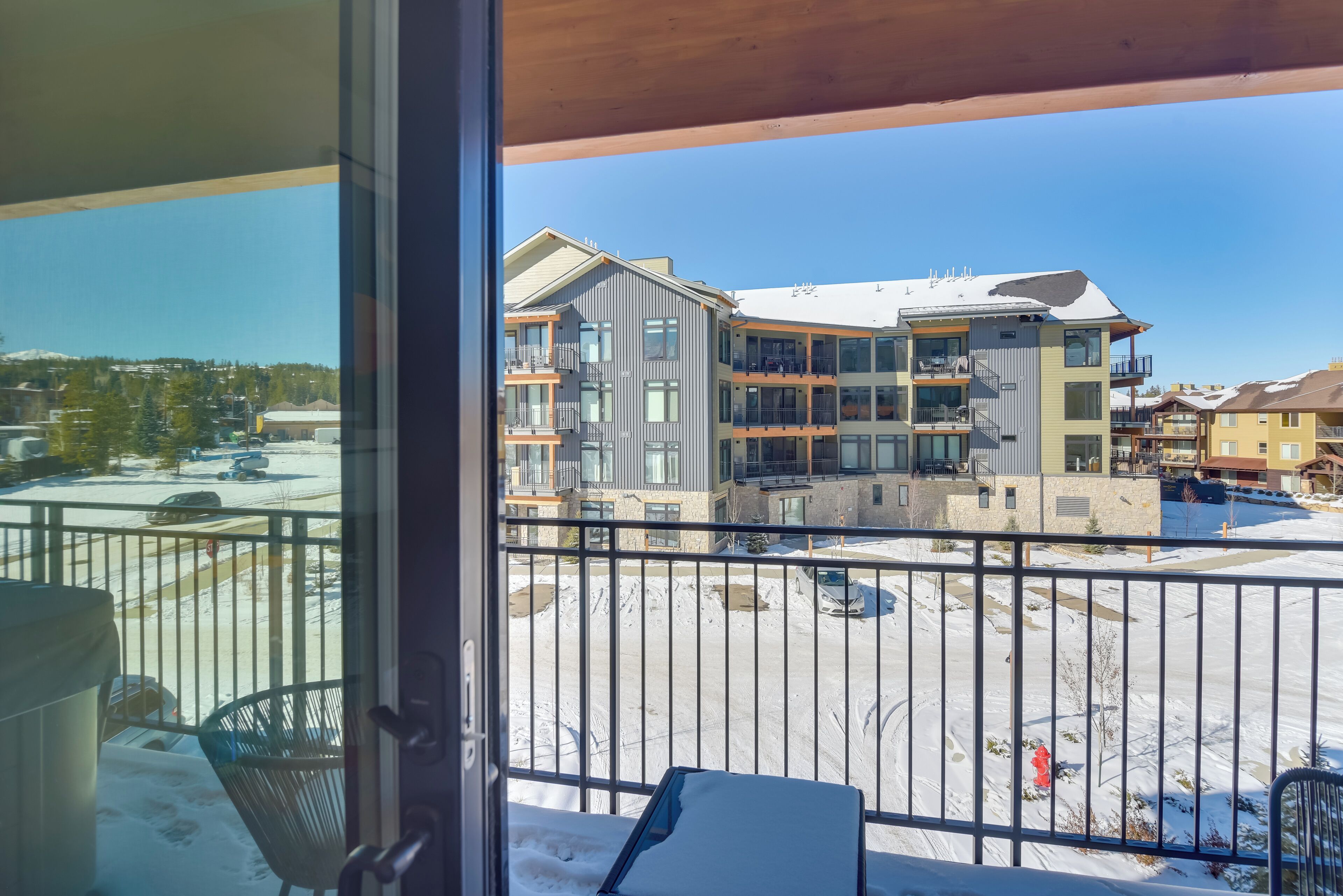 A balcony with a view of a multi-story building with balconies and a parking area covered in snow.