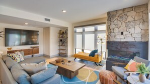 A modern living room with a large flat-screen TV, comfortable seating, a stone accent wall, and a fireplace. - Winter Park Condo w/ Hot Tub, Balcony & Shuttle! (Winter Park)