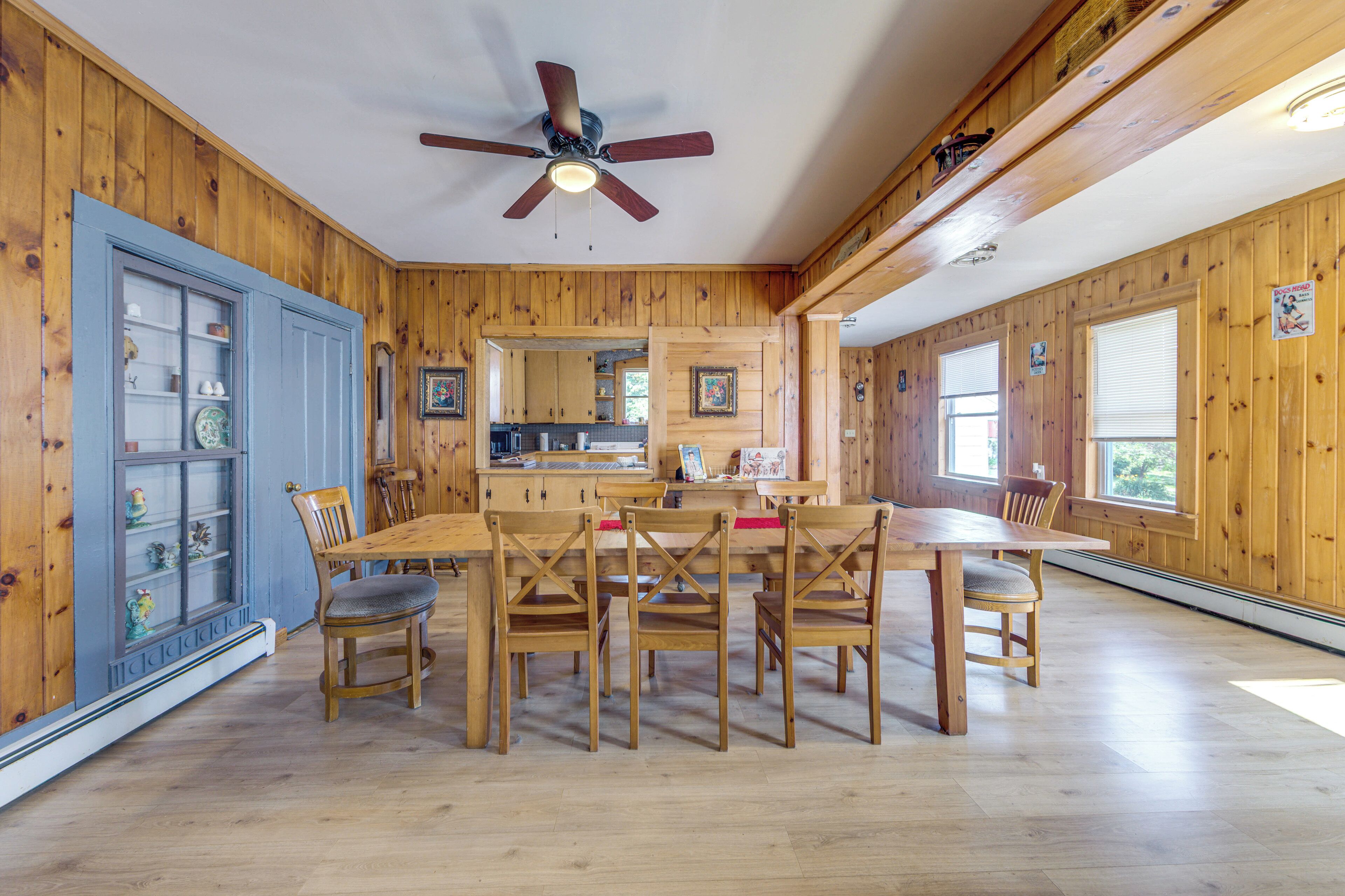 A wooden-paneled room with a dining table and chairs, a ceiling fan, and a kitchen area.