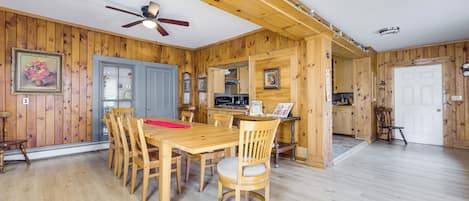 A wooden interior with a dining table, chairs, a ceiling fan, and a kitchen area.