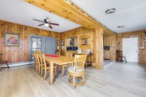 Un intérieur en bois comprenant une table à manger, des chaises, un ventilateur de plafond et un coin cuisine.