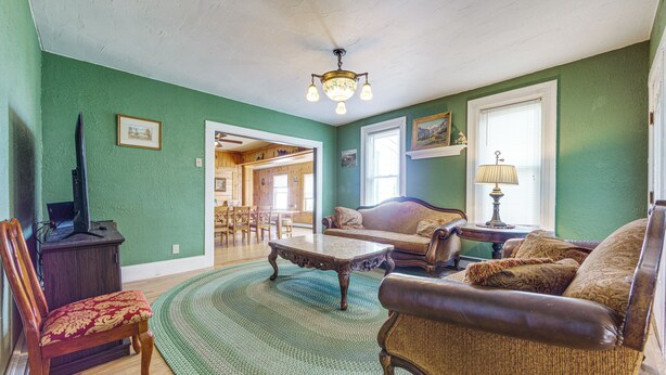 A living room with a green wall, a wooden floor, a sofa, a coffee table, a lamp, and a chair. - Altmar Vacation Rental ~ 4 Mi to Salmon River! (Parish)
