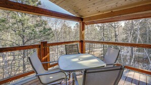 A covered outdoor deck with a table and chairs, surrounded by a wooden railing and overlooking a forested area. - Ride to Sturgis! Lead Home w/ Pool Access (Lead)