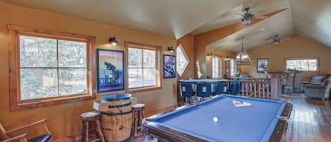 A pool room with wooden flooring, a pool table, and bar stools.