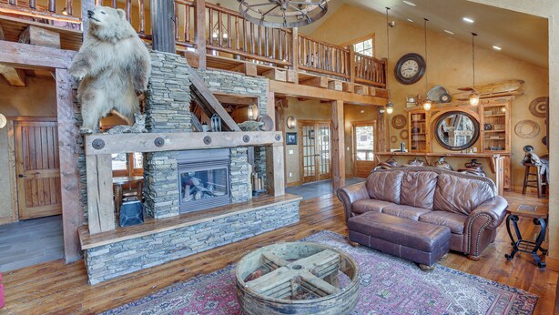 A spacious living area with a stone fireplace, wooden furniture, and a bear statue. - Ride to Sturgis! Lead Home w/ Pool Access (Lead)