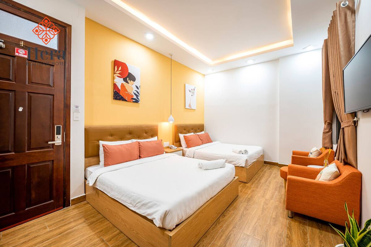 A hotel room with two beds, a TV, a sofa, and artwork on the wall.