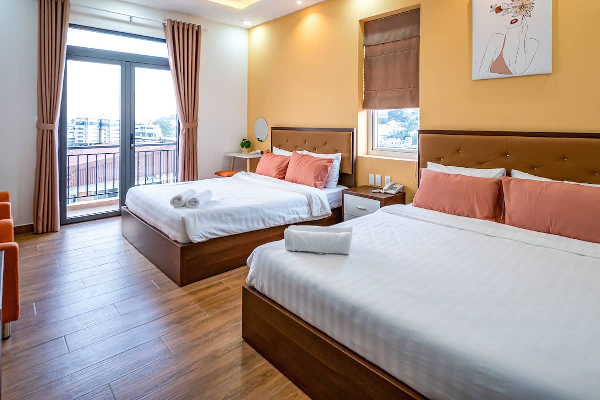 A hotel room with two beds, a sitting area, and a balcony with curtains.