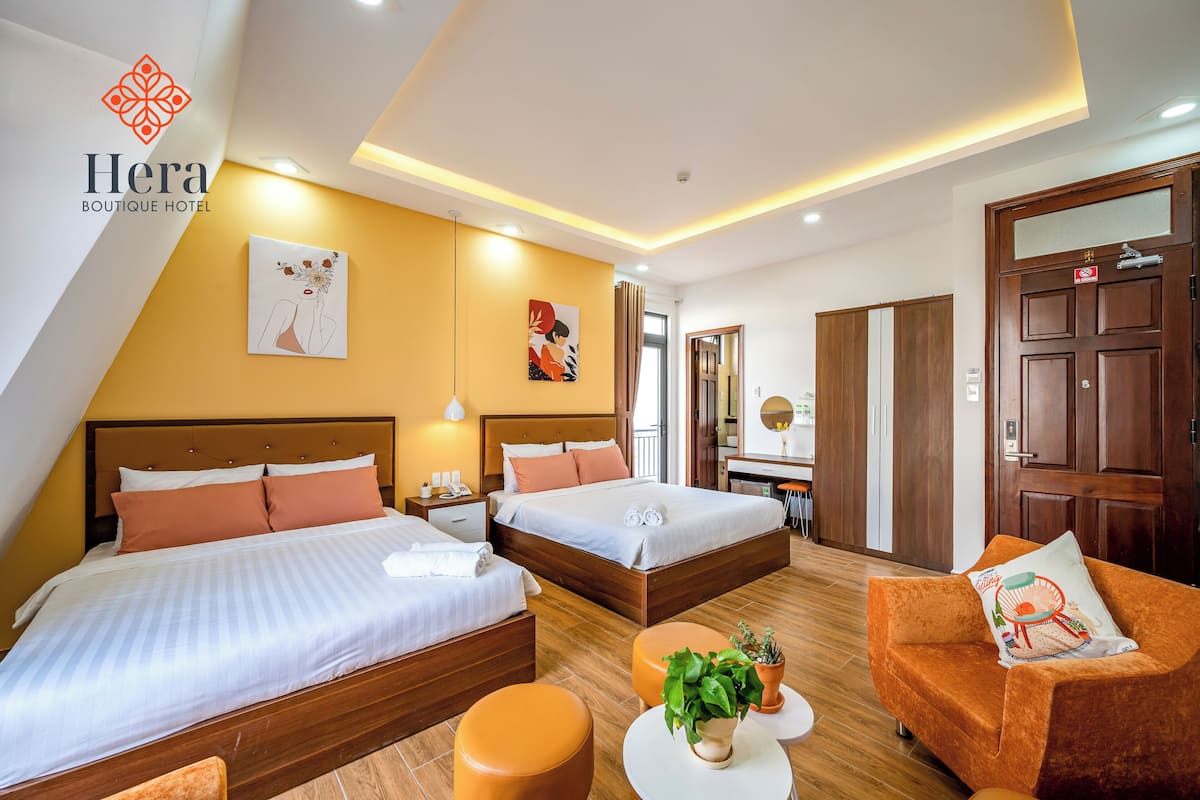A hotel room with two beds, a sofa, a small table with a plant, and a mirror.