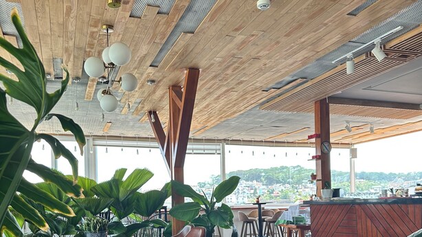 A restaurant with wooden ceiling beams, large windows, and lush indoor plants. - Hera Boutique Hotel (Xuan Huong - Da Lat)