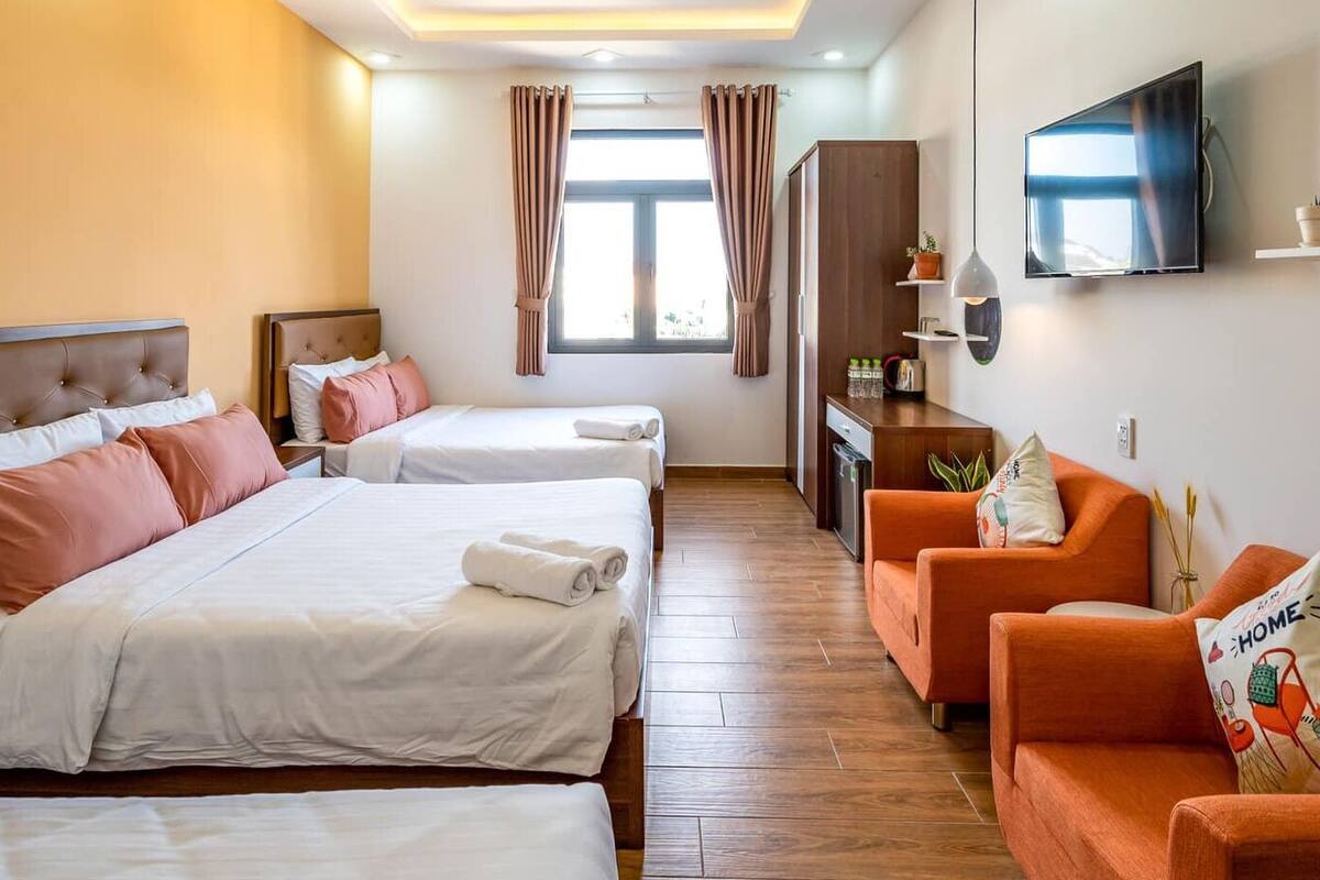 A hotel room with two beds, a sofa, a TV, and a small kitchen area.