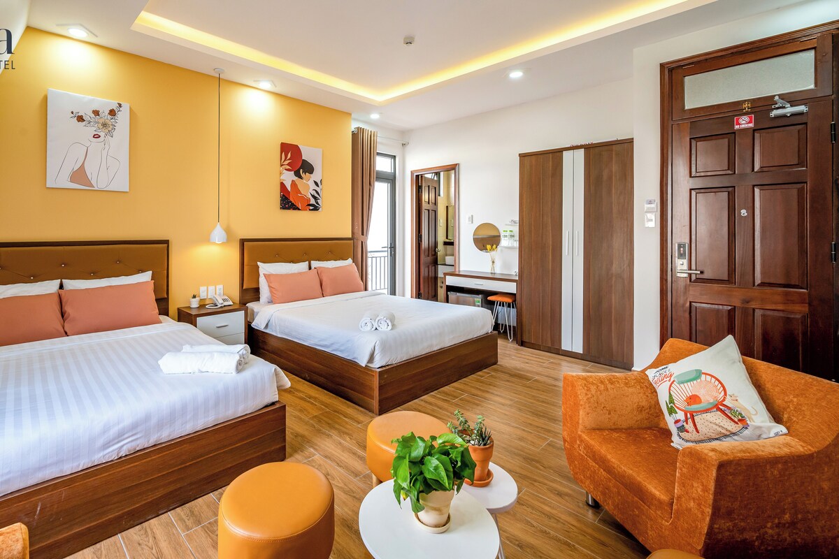 A hotel room with two beds, a sofa, a small table with a plant, and a mirror.