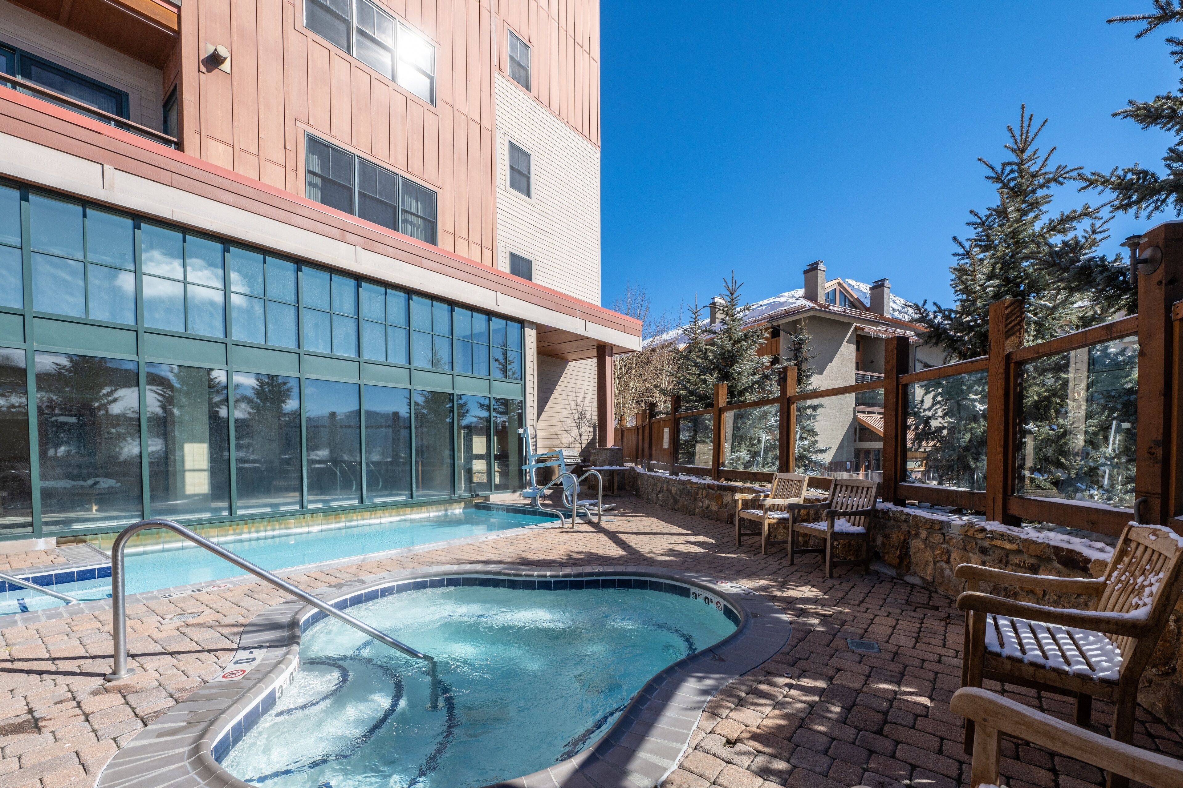 A pool area with a hot tub, outdoor seating, and a view of a building with large windows.