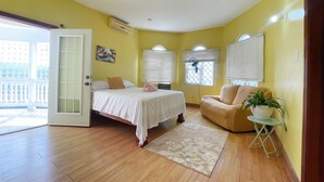 Quarto com cama, uma cadeira, uma mesinha com uma planta e uma janela com persianas.