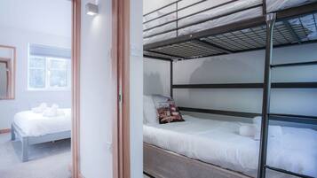 Une chambre avec un lit superposé, un lit simple et une fenêtre avec des stores.
