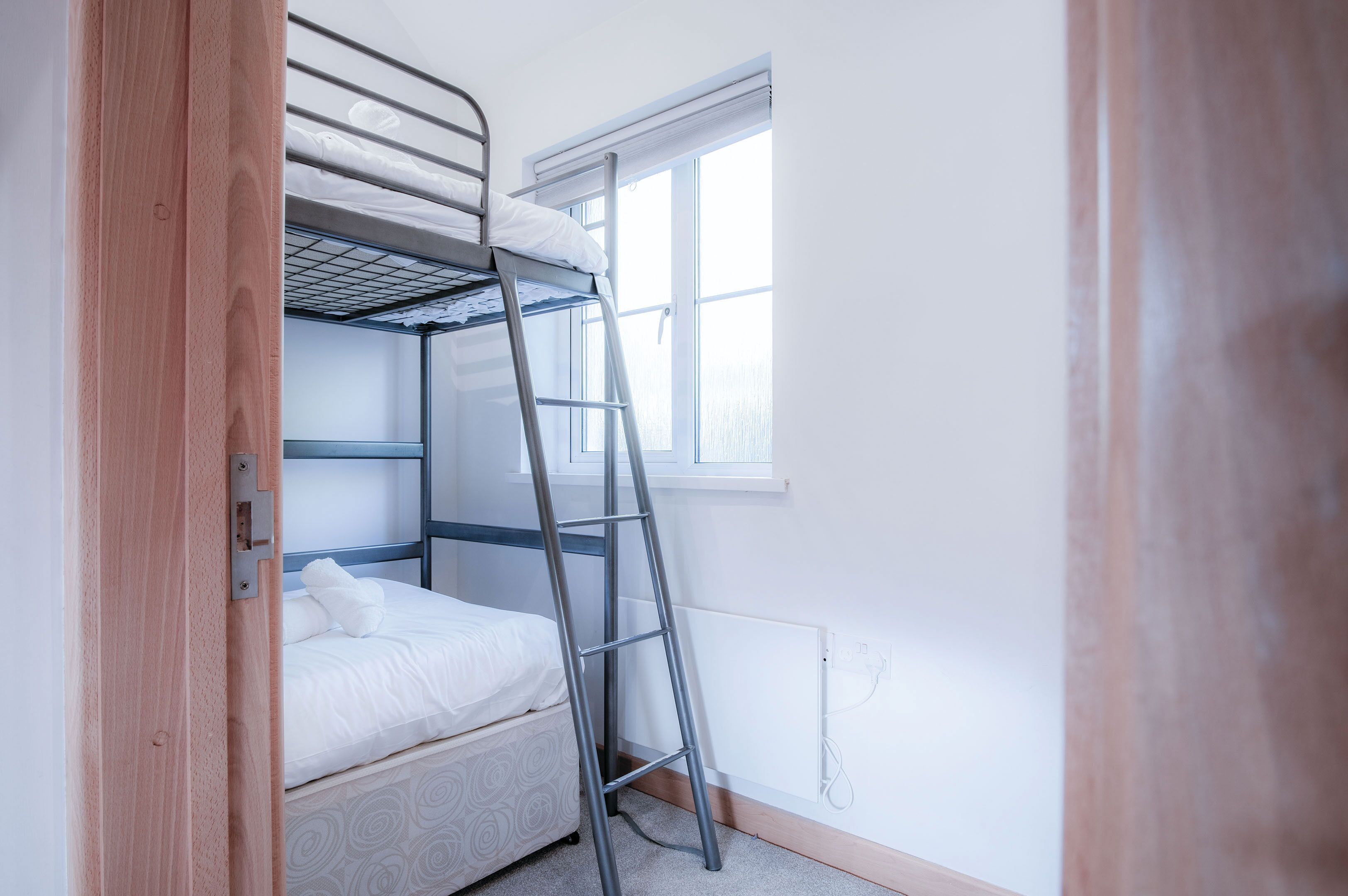 A bunk bed with a ladder, a window, and a door.